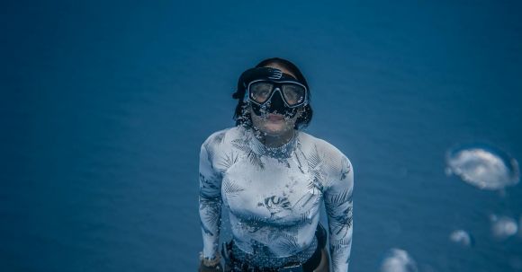 Wetsuit - From above of anonymous female diver in flippers wearing white swimsuit rising from deep water with bubbles in sea